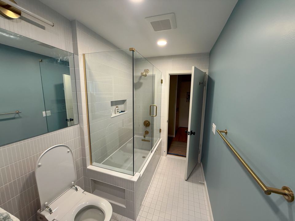 Finished bathroom with glass tub enclosure and brass fixtures