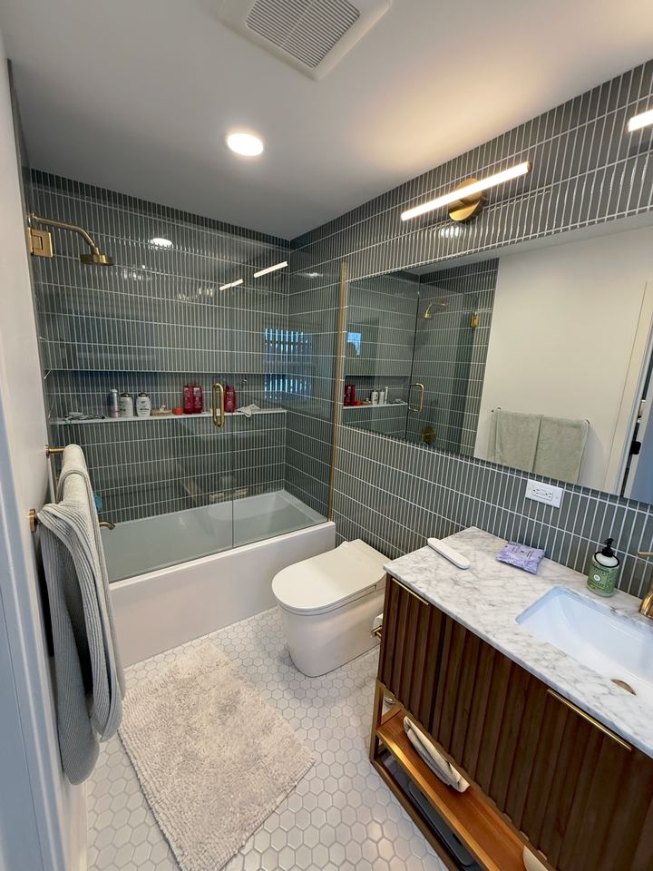Finished bathroom with green tile tub surround and wood vanity